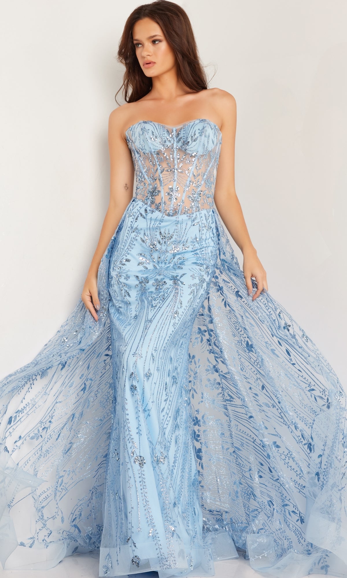 A woman models the Jovani Strapless Long Glitter-Sequin Prom Dress 26113, featuring a sheer corset-style bodice with silver embroidery and a light blue mermaid skirt, set against a plain background.